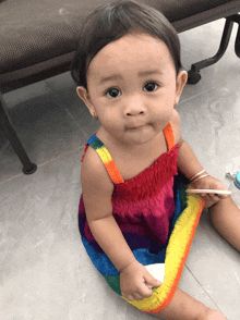 a baby girl wearing a rainbow dress is sitting on the floor