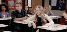 a boy and a girl are sitting at desks in a classroom with other students .