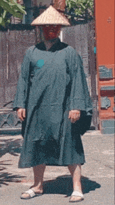 a man wearing a conical hat and a green robe stands in front of a red door with the number 2 on it