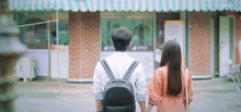 a man and a woman are walking in front of a building holding hands .
