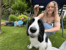 a woman petting a black and white dog while a man lays on the grass