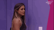 a woman is laughing in front of a purple wall that says apowerrec big brother brasil