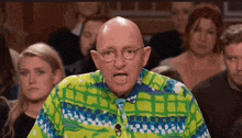 a bald man wearing glasses and a colorful shirt stands in front of a crowd .