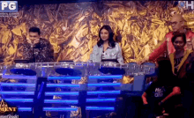 a group of people are sitting at a table on a stage in front of a gold wall .