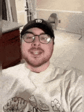 a man wearing glasses and a hat is taking a selfie in a room .