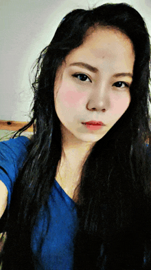 a woman with long black hair is wearing a blue shirt and taking a selfie