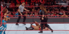 a woman is wrestling another woman in a wrestling ring while a referee stands behind her .