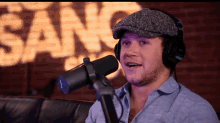 a man wearing headphones and a hat is singing into a microphone in front of a sign that says sang