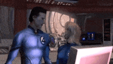 a man and a woman in superhero costumes are standing next to each other in front of a computer .