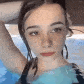 a woman in a bathing suit is swimming in a pool and looking at the camera .