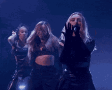 a woman singing into a microphone while two other women dance