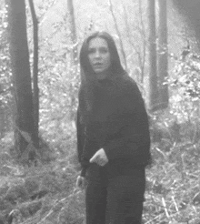 a woman in a black jacket is standing in a forest