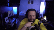a man wearing headphones and a yellow shirt is sitting in front of a microphone in a room