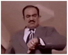 a man in a suit and tie is looking at his watch and making a funny face .