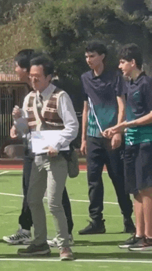 a group of young men are standing on a tennis court with a man holding a piece of paper .