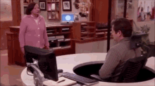 a woman in a pink sweater is standing next to a man in a wheelchair at a desk .