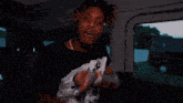 a young man with dreadlocks is sitting in a car and making a funny face .