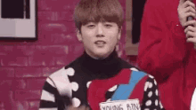 a young man wearing a colorful sweater is standing in front of a brick wall .