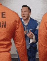 a man in a blue suit and tie is standing next to a man in an orange uniform with the letter e on the back
