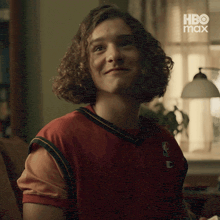 a young man with curly hair is sitting on a couch wearing a basketball jersey .