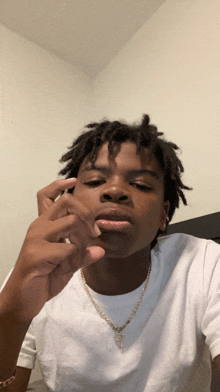 a young man with dreadlocks is wearing a white shirt and a gold chain