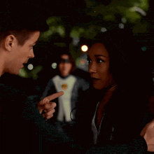 a man and a woman are talking to each other while a man in a suit is standing in the background .