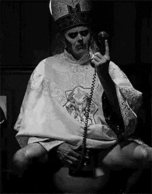 a man in a priest 's robe is sitting on a toilet .