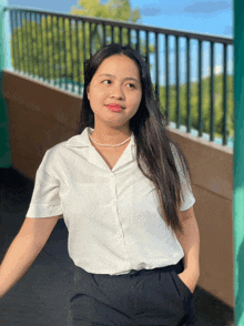 a woman wearing a white shirt and black pants stands in front of a green railing