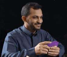 a man in a blue shirt is holding a purple piece of paper .
