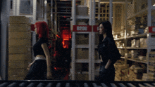 two women standing in a warehouse with a red sign that says r206