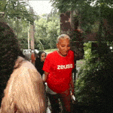 a woman wearing a red zeus t-shirt stands in the woods