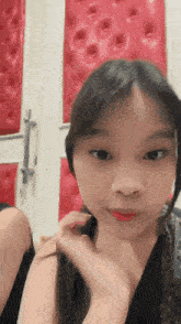 a young girl is looking at the camera with a red wall behind her