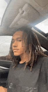 a young man with dreadlocks is sitting in a car wearing a black t-shirt that says 2nite223 on it