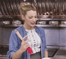 a woman in a denim jacket is holding a red spatula in a kitchen .