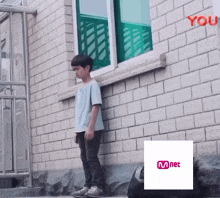 a young boy leaning against a brick wall next to a mnet sign