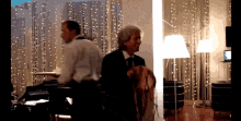 a man in a suit and tie stands in a room with a lamp