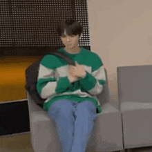 a man in a green and white striped sweater is sitting in a chair with a backpack .