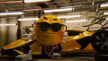 a yellow smiley face wearing sunglasses is standing next to a yellow sports car .