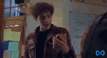 a young man with curly hair is looking at his cell phone in a classroom .