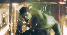 the hulk is standing on a rock in a room with sparks coming out of him .