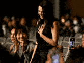 a woman in a black dress stands in front of a group of people and the word filmatrice is on the bottom right