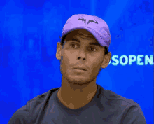 a man wearing a purple hat is sitting in front of a blue screen that says sopen