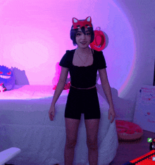 a girl wearing a cat mask stands in front of a bed and a keyboard