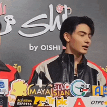 a man in a leather jacket is standing in front of a sign that says oishi .