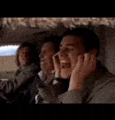 a man is covering his ears with his hands while sitting in a car with other men .