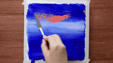 a person is using a knife to spread paint on a blue surface
