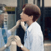 a man in a white shirt is looking at his reflection in the glass