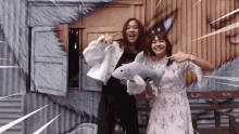 two women are standing next to each other holding a stuffed shark and pointing at it .
