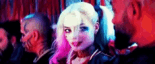 a woman with pink hair is standing next to a man with a tattoo on his face in a dark room .