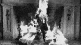 a black and white photo of a man standing in front of a fireplace on fire .